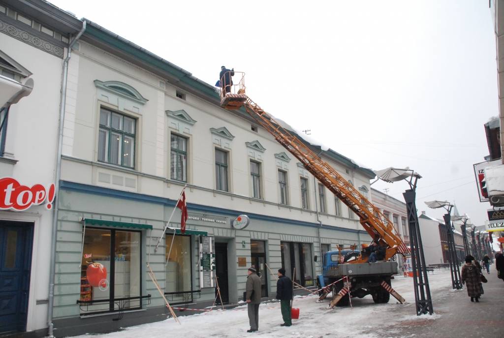 Valsts Nekustamo īpašumu aģentūra no apsaimniekojamo namu jumtiem Tirgoņu ielā novāc sniegu, kas bīstami pārkāries pāri jumta malai.